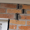 A brick wall displaying stair-step cracks and messy tuckpointing on a Laramie home